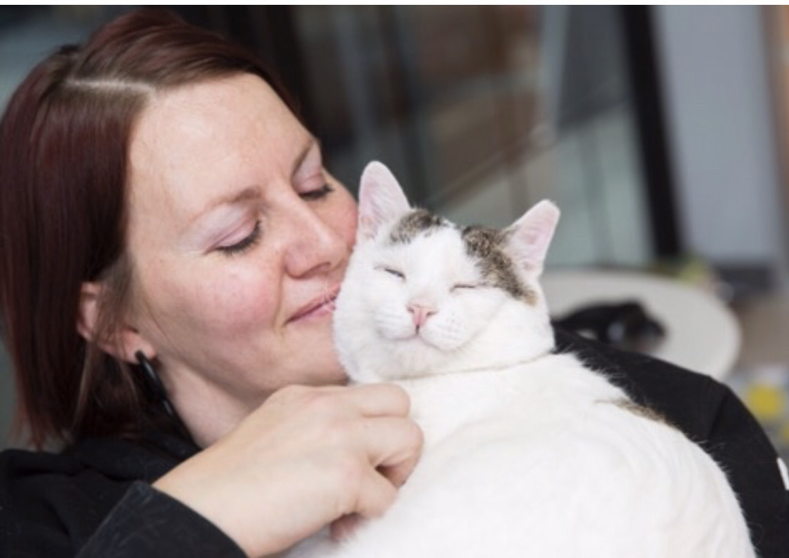 Whiskers founder Jessica Vigos snuggles a content looking white cat with a speckled grey pattern on his crown. The pair seems comfortable.